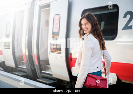 Porträt einer Geschäftsfrau, die mit Handgepäck in einem Bahnhof oder Flughafen zum Boarding Gate geht Stockfoto
