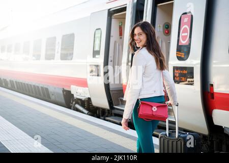 Porträt einer Geschäftsfrau, die mit Handgepäck in einem Bahnhof oder Flughafen zum Boarding Gate geht Stockfoto