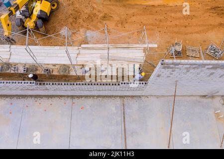Gerüste auf der Baustelle werden Arbeiter gesehen, wie sie Ziegelsteine aus gemauerten Zinnbetonblöcken legen Stockfoto