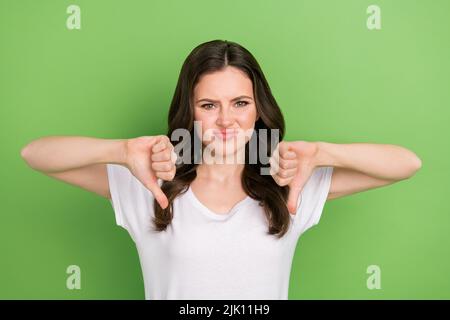 Foto von unglücklich verärgert junge Dame tragen weißes T-Shirt zeigt zwei Daumen nach unten isoliert grünen Hintergrund Stockfoto