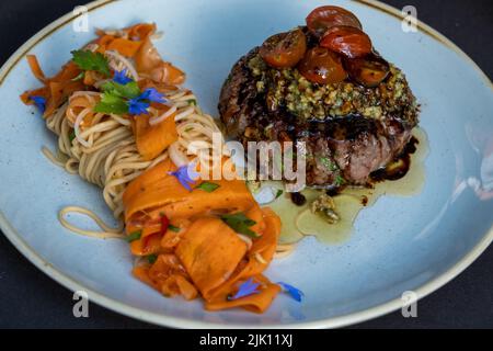 Gegrilltes Rindersteak mit Pasta, Tomaten und Karotten auf einem Teller isoliert auf schwarzem Hintergrund. Stockfoto