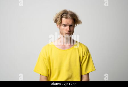 Nahaufnahme Porträt eines wütenden jungen Mannes. Porträt eines verärgerten jungen Mannes ein gelbes T-Shirt, das mit isolierten Armen auf weißem Hintergrund steht. Emotion von Stockfoto