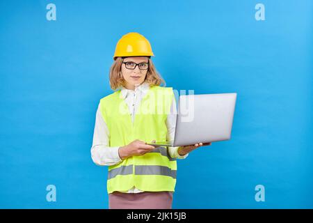 Studio-Aufnahme der weiblichen professionellen Engineering-Vorarbeiter Manager tragen harten Helm und reflektierende Schutzweste stehen und lächeln, halten Laptop comput Stockfoto