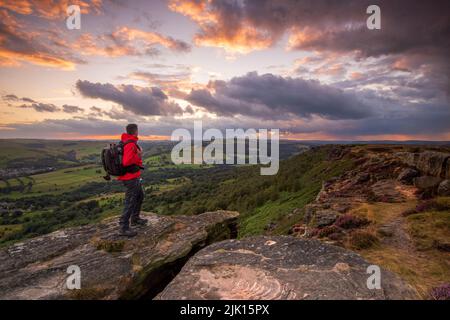 Ein männlicher Wanderer, der bei Sonnenuntergang auf Curbar Edge, Peak District, Derbyshire, England, Großbritannien, Europa Stockfoto