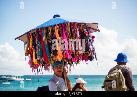 Straßenverkäufer laufen auf dem Sand des Strandes Porto da Barra in Salvador, Bahia. Stockfoto