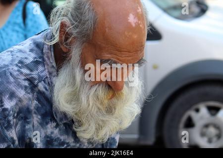 Ein alter Mann mit einem langen weißen Bart geht die Straße entlang, wobei der Kopf nach unten nachdenklich aussieht Stockfoto