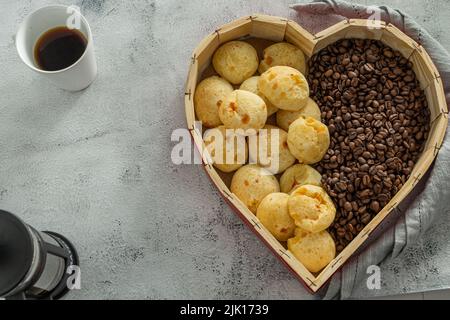 Brasilianisches Käsebrot oder Käsebrot in einem herzförmigen Korb mit Kaffeebohnen auf einer Marmor- oder Steinoberfläche Stockfoto