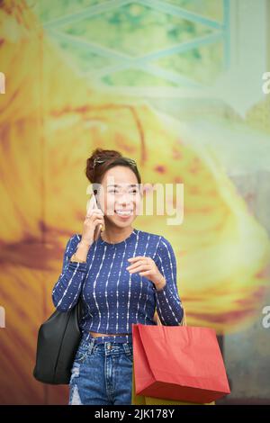 Glückliche asiatische junge Frau mit Papiertüten, die am Telefon anrufen Stockfoto