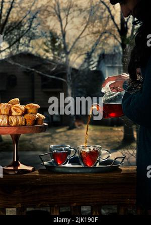 Frauen gießen Tee aus einer transparenten Teeschale zu einer Tasse auf einer Holzoberfläche in einer wunderschönen Natur draußen Stockfoto