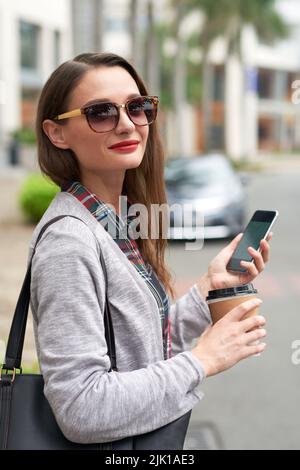 Modische junge Frau mit Smartphone und Kaffee Stockfoto