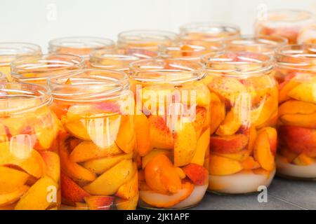Nahaufnahme von Aprikosenscheiben mit Wasser und Zucker in Gläsern. Hausgemachte Fruchtkompott, fertig zum Verlecken und Sterilisieren. Vorbereitung der Wintervorräte zu Hause. Stockfoto
