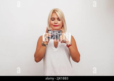 Frau mittleren Alters mit weißem Haar hält eine Vintage-Kamera in den Händen Stockfoto