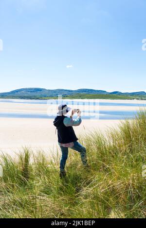 Die Frau fotografiert mit der Telefonkamera am Ballinreavy Strand neben dem Sheskinmore Nature Reserve. Sheskinmore bezieht sich auf ein großes Gebiet von Sanddünen, See und Stockfoto