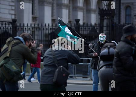 Eine Person, die eine Maske trägt, wird während eines „Cost of Living Crisis“-Protestes in der Nähe der Downing Street in London von Fotografen umgeben. Stockfoto