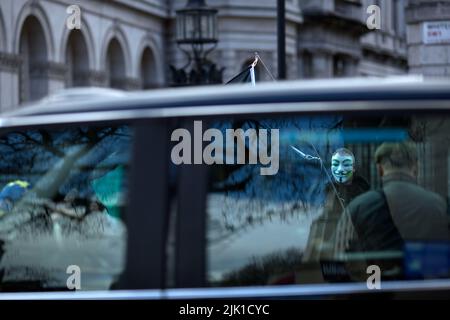 Eine Person, die eine Maske trägt, wird während eines „Cost of Living Crisis“-Protestes in der Nähe der Downing Street in London von Fotografen umgeben. Stockfoto