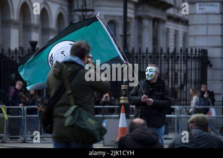 Eine Person, die eine Maske trägt, wird während eines „Cost of Living Crisis“-Protestes in der Nähe der Downing Street in London von Fotografen umgeben. Stockfoto