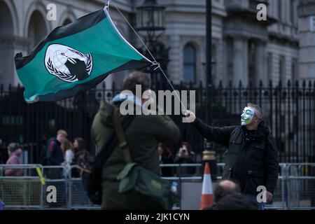 Eine Person, die eine Maske trägt, wird während eines „Cost of Living Crisis“-Protestes in der Nähe der Downing Street in London von Fotografen umgeben. Stockfoto