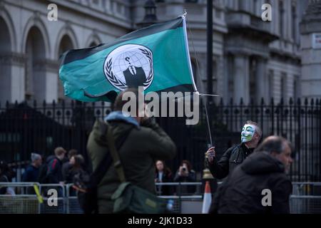 Eine Person, die eine Maske trägt, wird während eines „Cost of Living Crisis“-Protestes in der Nähe der Downing Street in London von Fotografen umgeben. Stockfoto