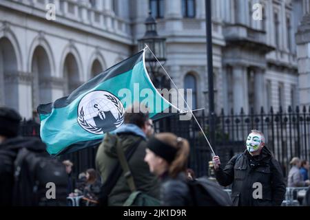 Eine Person, die eine Maske trägt, wird während eines „Cost of Living Crisis“-Protestes in der Nähe der Downing Street in London von Fotografen umgeben. Stockfoto