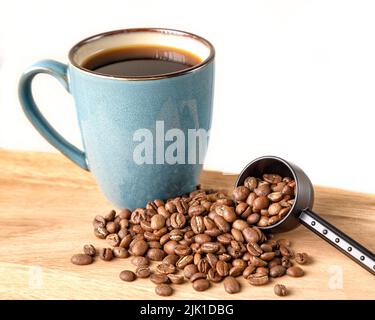 Kaffeebohnen, die aus einer Kugel mit einem grünen Becher Kaffee verschüttet werden Stockfoto