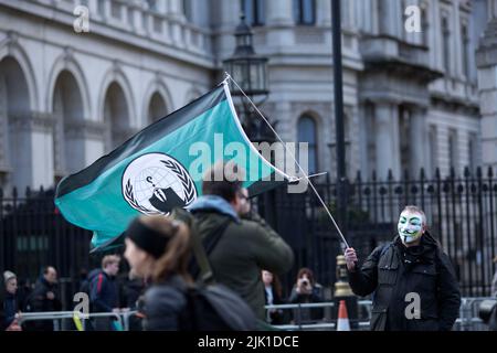 Eine Person, die eine Maske trägt, wird während eines „Cost of Living Crisis“-Protestes in der Nähe der Downing Street in London von Fotografen umgeben. Stockfoto