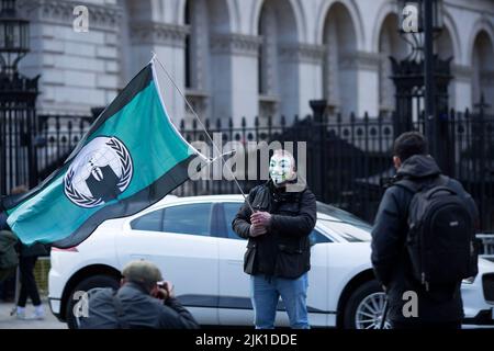 Eine Person, die eine Maske trägt, wird während eines „Cost of Living Crisis“-Protestes in der Nähe der Downing Street in London von Fotografen umgeben. Stockfoto