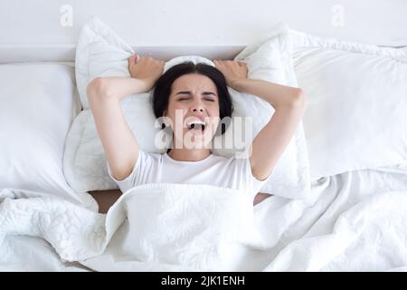 Frustriert und verärgert Frau im Bett allein zu Hause weinend und schreiend, Draufsicht, brünett in weißen T-Shirt Pyjamas liegen Stockfoto