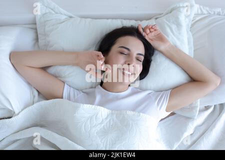 Draufsicht, junge schöne Brünette Frau schlafen im Bett mit geschlossenen Augen, lächelnd im Schlaf tragen weißen T-Shirt Pyjamas Stockfoto