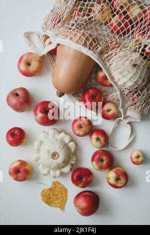 Herbsternte mit Quadratwurz, Kürbis, Äpfeln und Gemüse in einer Mesh-Einkaufstasche auf weißem Hintergrund Stockfoto