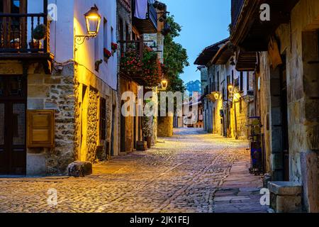 Enge Gasse der alten Steinstadt mit gepflasterten Straßen, die nachts beleuchtet sind. Stockfoto