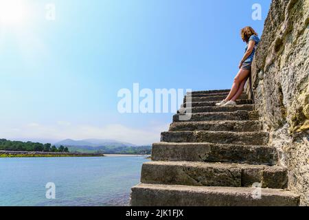 Frau oben auf einigen Treppen, die an sonnigen Tagen auf den Strand schaute. Stockfoto