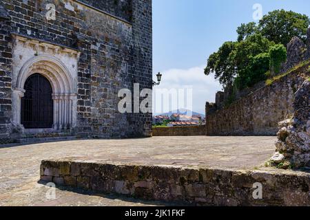 Mittelalterliche Kirche mit gewölbter Eingangstür und Häusern in der Ferne. Suances Santander. Stockfoto