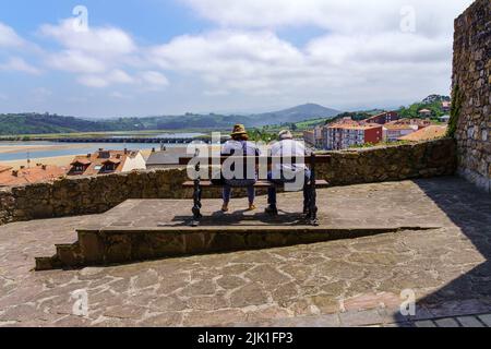 Zwei Menschen ruhen sich auf einer Holzbank aus und betrachten die Landschaft. San Vicente de la Barquera. Stockfoto