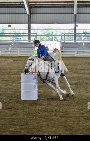 Eine junge Reiterin auf einem weißen Pferd tritt bei einem Barrel-Rennen auf der Delaware State Fair in Harrington, Delaware USA, an. Stockfoto