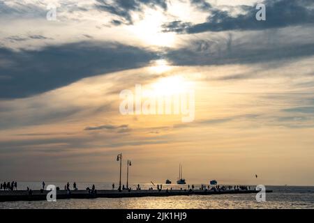 Triest, Italien, 28. Juli 2022. Die Menschen genießen den Sonnenuntergang am Molo Audace (Audace Pier) vor der größten Segelyacht der Welt (C) und zwei Crui Stockfoto