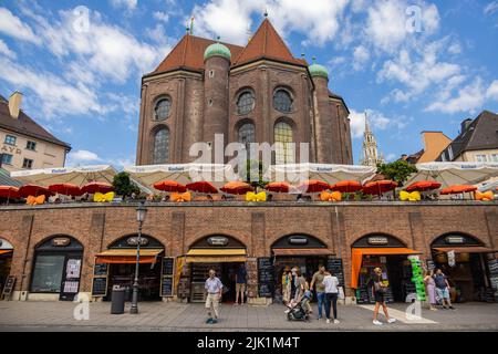 München, 6. Juli 2022: Blick vom Viktualienmarkt auf die Peterskirche oder die Peterskirche. Die Geschäfte von verschiedenen Metzgern in der Vorgruppe Stockfoto