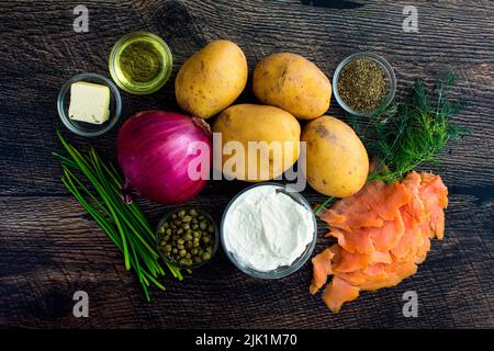 Zutaten für einen Kartoffelkuchen mit geräuchertem Lachs und Labneh: Blick von oben auf Goldkartoffeln, Nova, Kapern und andere Rohstoffe Stockfoto