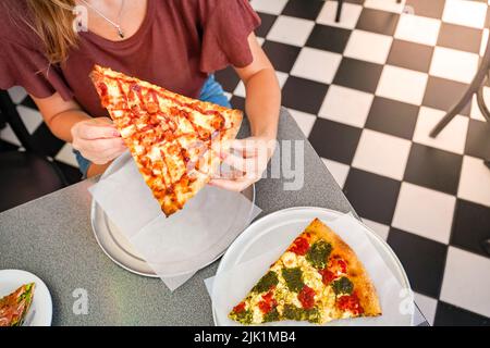Nahaufnahme unkenntliche Freunde essen köstliche Pizzastücke drinnen. Stockfoto