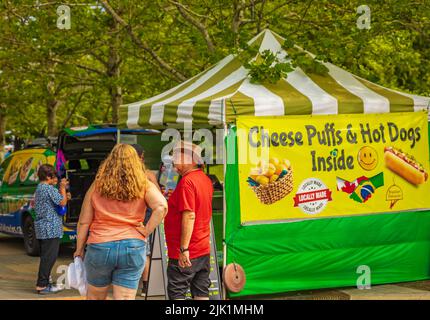 Menschen, die auf dem Markt in einem Park Essen und Getränke im Freien kaufen, essen und kaufen. Marktstände. Markt im Freien. Food-Event. Food Fair. Festival. Floh Stockfoto