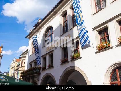 München, Deutschland - 6. Juli 2022: Die Königliche Brauerei in München, das Münchener Hofbräuhaus am Platzl. Ein muss für Touristen. Die bayerische Flagge und das HB-Logo Stockfoto