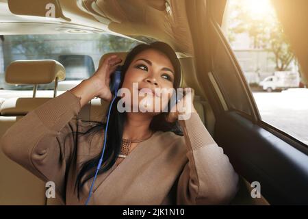 Schöne vietnamesische Frau, die im Auto sitzt und ihrer Lieblingsmusik lauscht Stockfoto