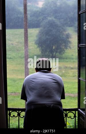 Mann schaut durch das Fenster, Regen Stockfoto