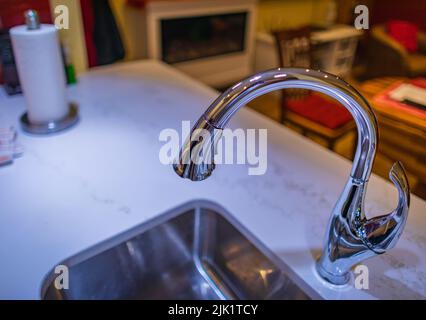 Küchenmischer. Wasserhahn aus Chrom-Material. Marmorablagefläche und eingebautes Waschbecken mit silbernem Hahn. Niemand, verschwommen, selektiver Fokus, Zuhause Stockfoto