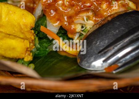 Javanesischer Salat aus frischem Gemüse und Gewürzen aus Erdnüssen, serviert auf einem Teller aus gewebtem Rattan Stockfoto