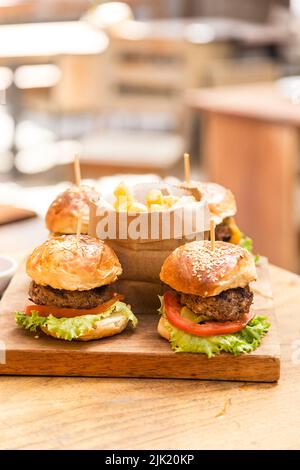 Vier Hamburger auf einem Holzbrett und pommes Frites in einem Holzpapierkorb in einem Restaurant Stockfoto