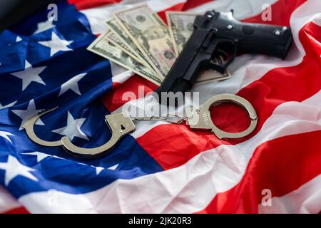 Handschellen der Polizei, Dollar und eine Waffe auf der US-Flagge, Nahaufnahme Stockfoto