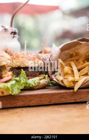 Burger, Pommes frites und ein Milchshake mit Rahm und Nüssen auf einem Holzbrett Stockfoto