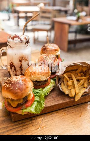 Burger, Pommes frites und ein Milchshake mit Rahm und Nüssen auf einem Holzbrett Stockfoto