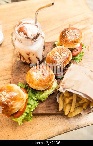 Burger, Pommes frites und ein Milchshake mit Rahm und Nüssen auf einem Holzbrett Stockfoto