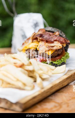 Cheeseburger mit Pilzen, Salat, Tomaten, Speck und Zwiebeln und pommes auf einem Holzbrett Stockfoto